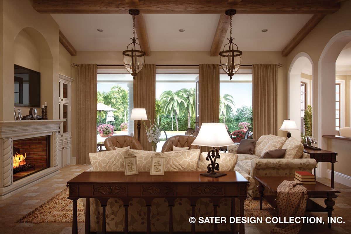 Living room with fireplace, beamed ceiling, and large windows opening to a patio with palm trees.