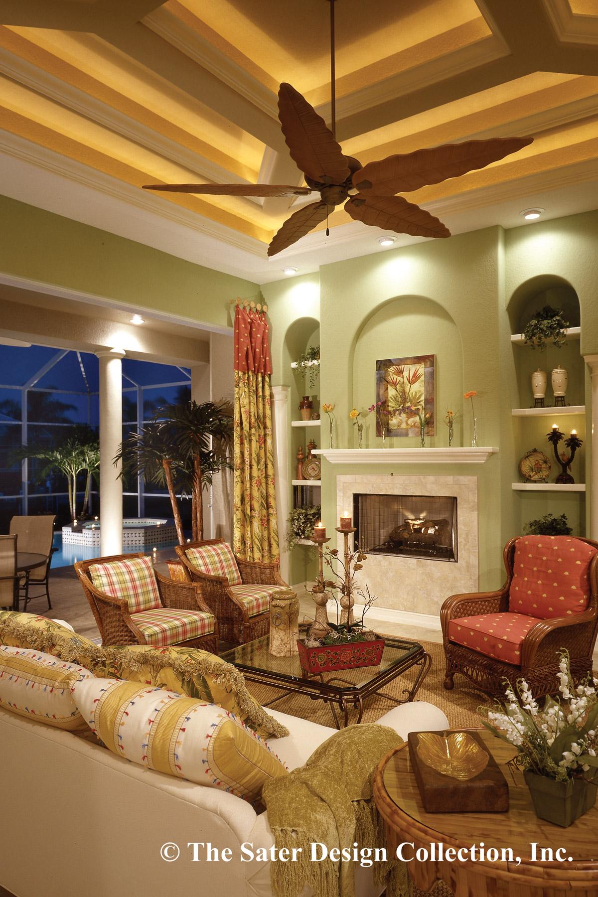 Living room with fireplace, patterned furniture, and tray ceiling with palm leaf fan. Doors open to pool area.