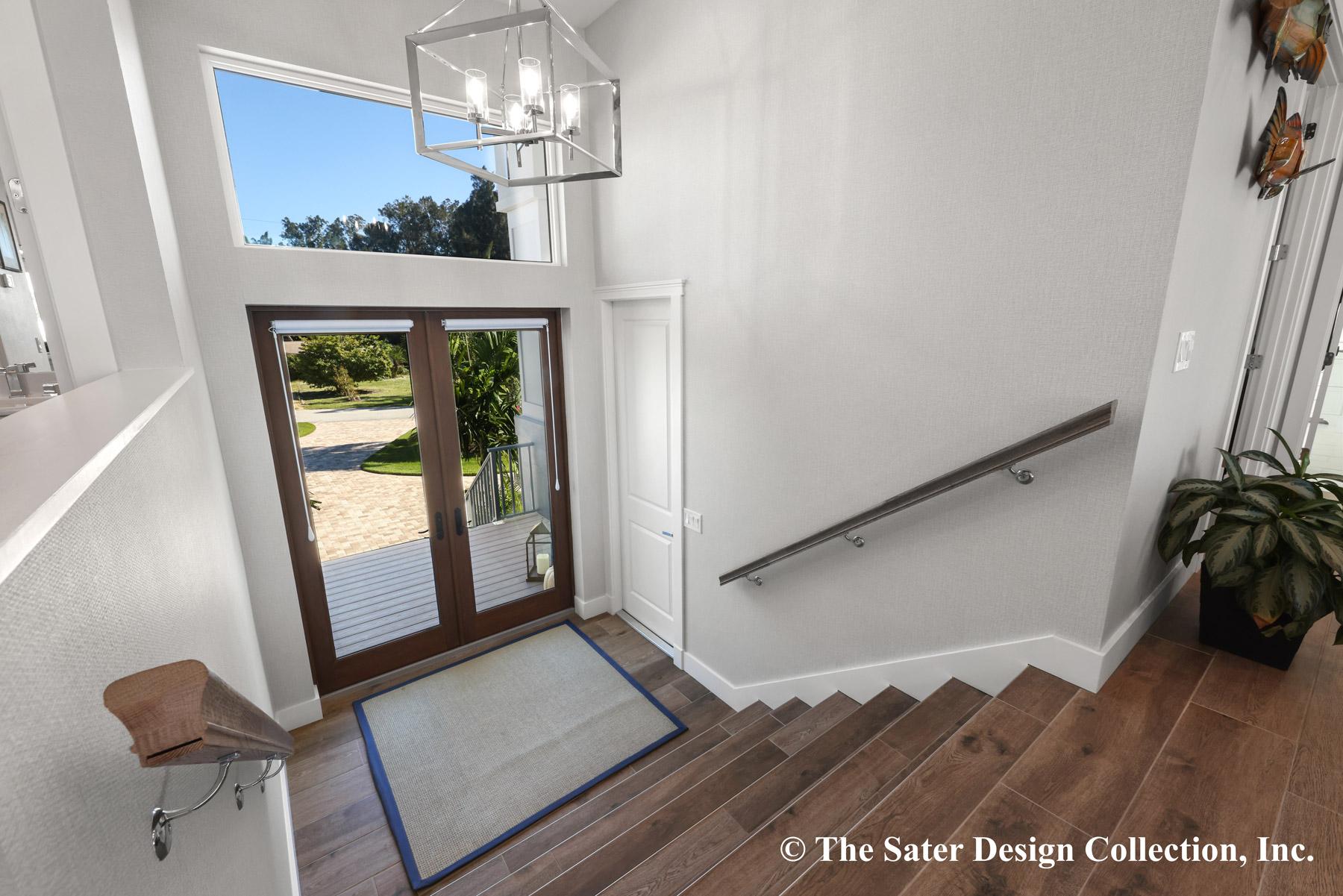 Entryway with double doors, a tall transom window, chandelier, and staircase with wood flooring and metal handrail.