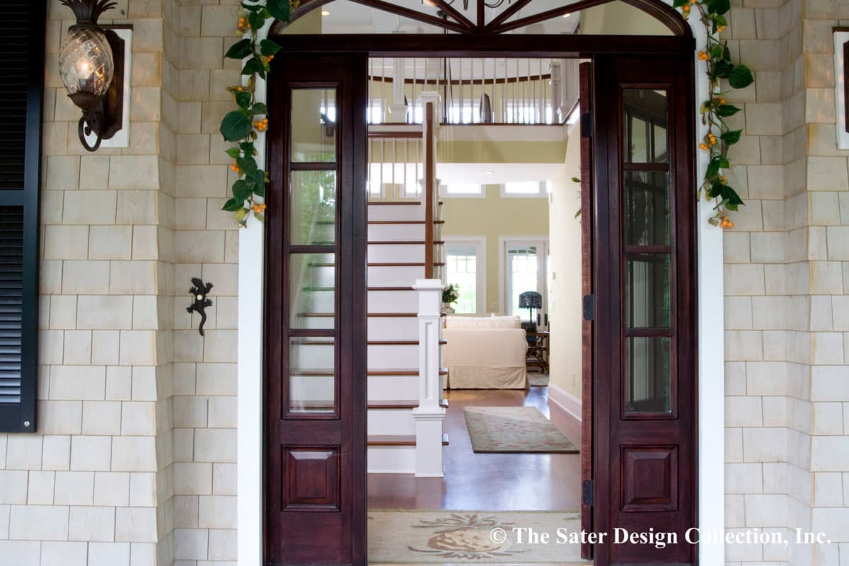 Entrance view of house plan: dark wood doors open to reveal a staircase and interior with light yellow walls and furniture.
