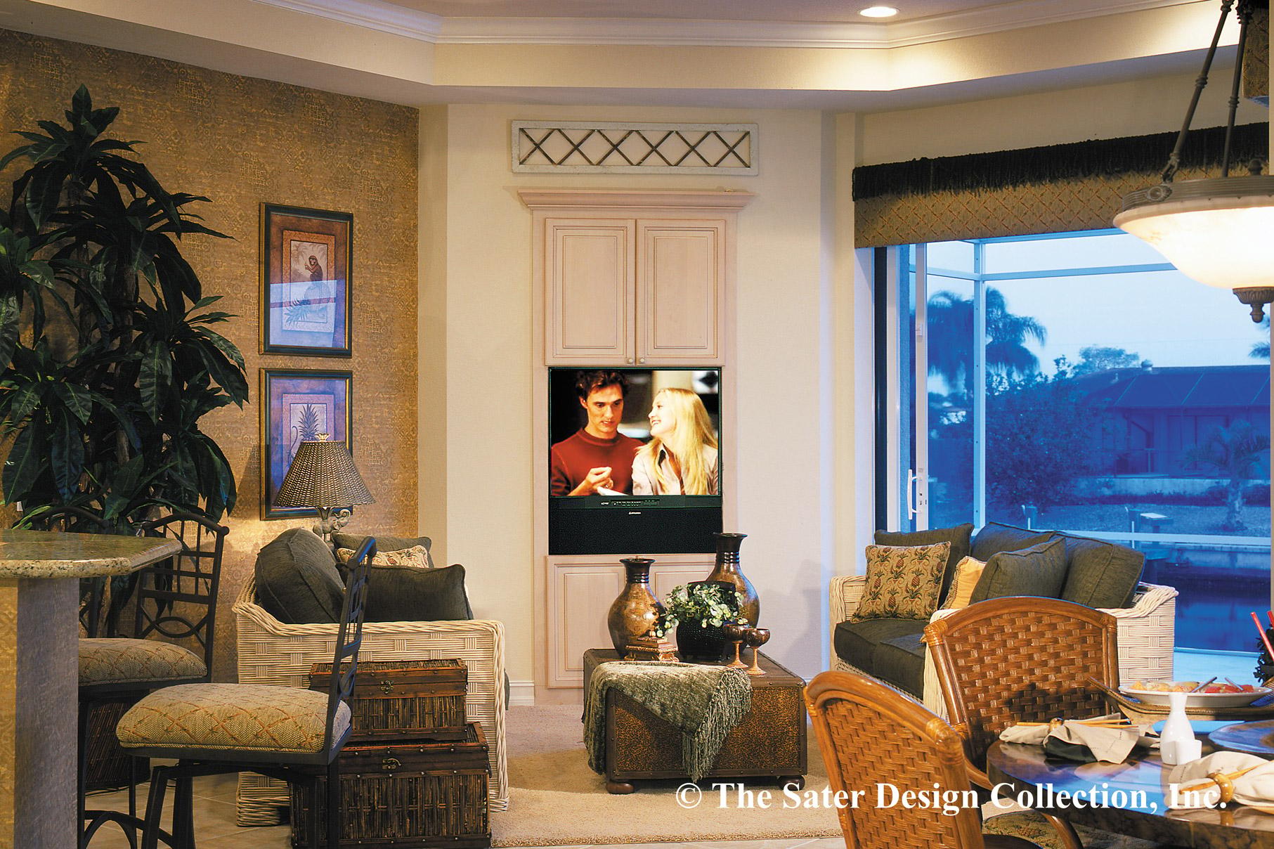 Living room with built-in entertainment center, large windows overlooking water, and wicker furniture.