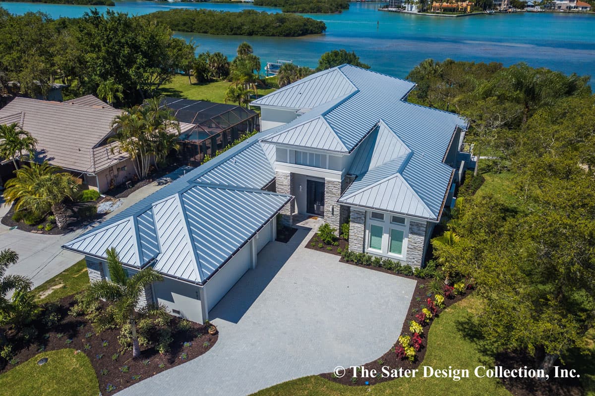 House plan exterior with standing seam metal roof, stone accents, attached three-car garage, and water views.