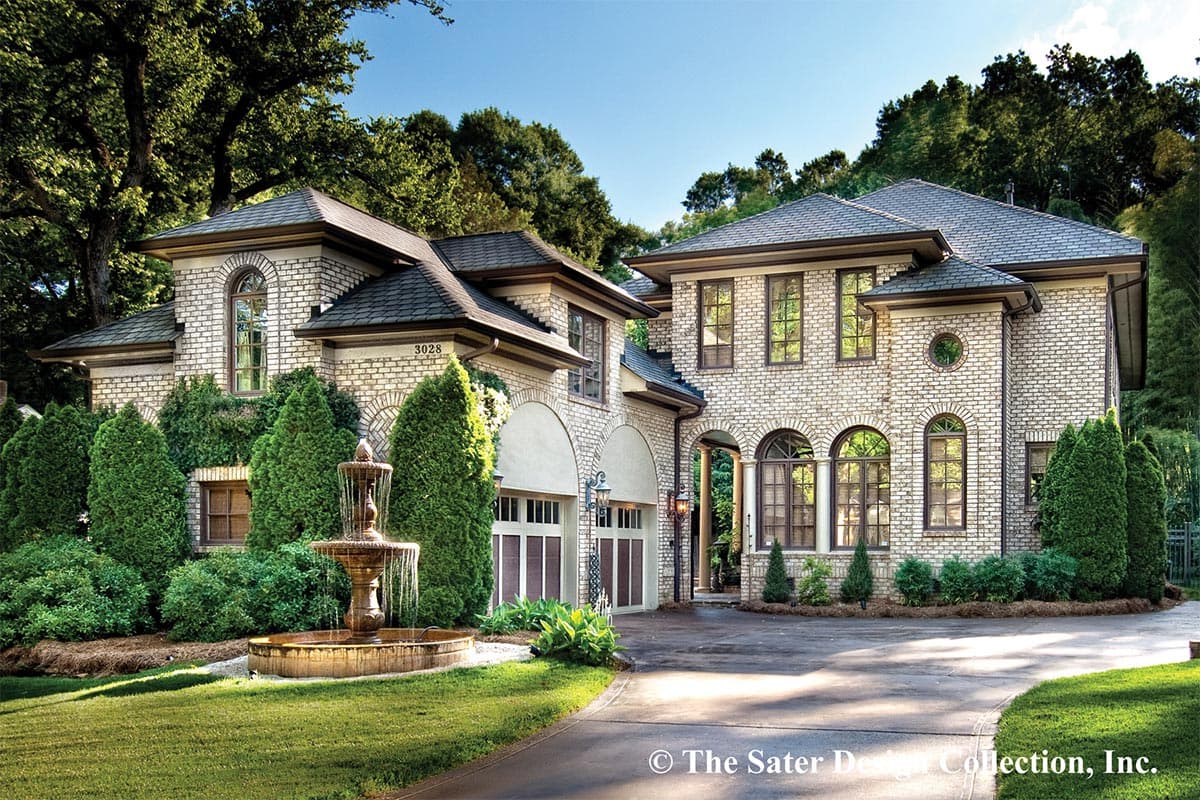 House plan exterior with two stories, brick facade, arched entry, multiple gables, and a porte-cochere. Features a fountain in the foreground.