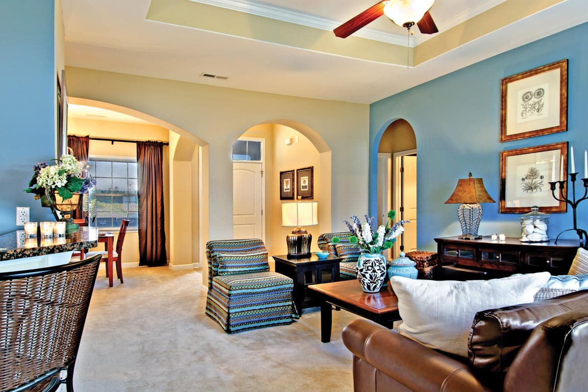 Interior rendering of a living room with arched doorways, a tray ceiling, and patterned accent chairs.