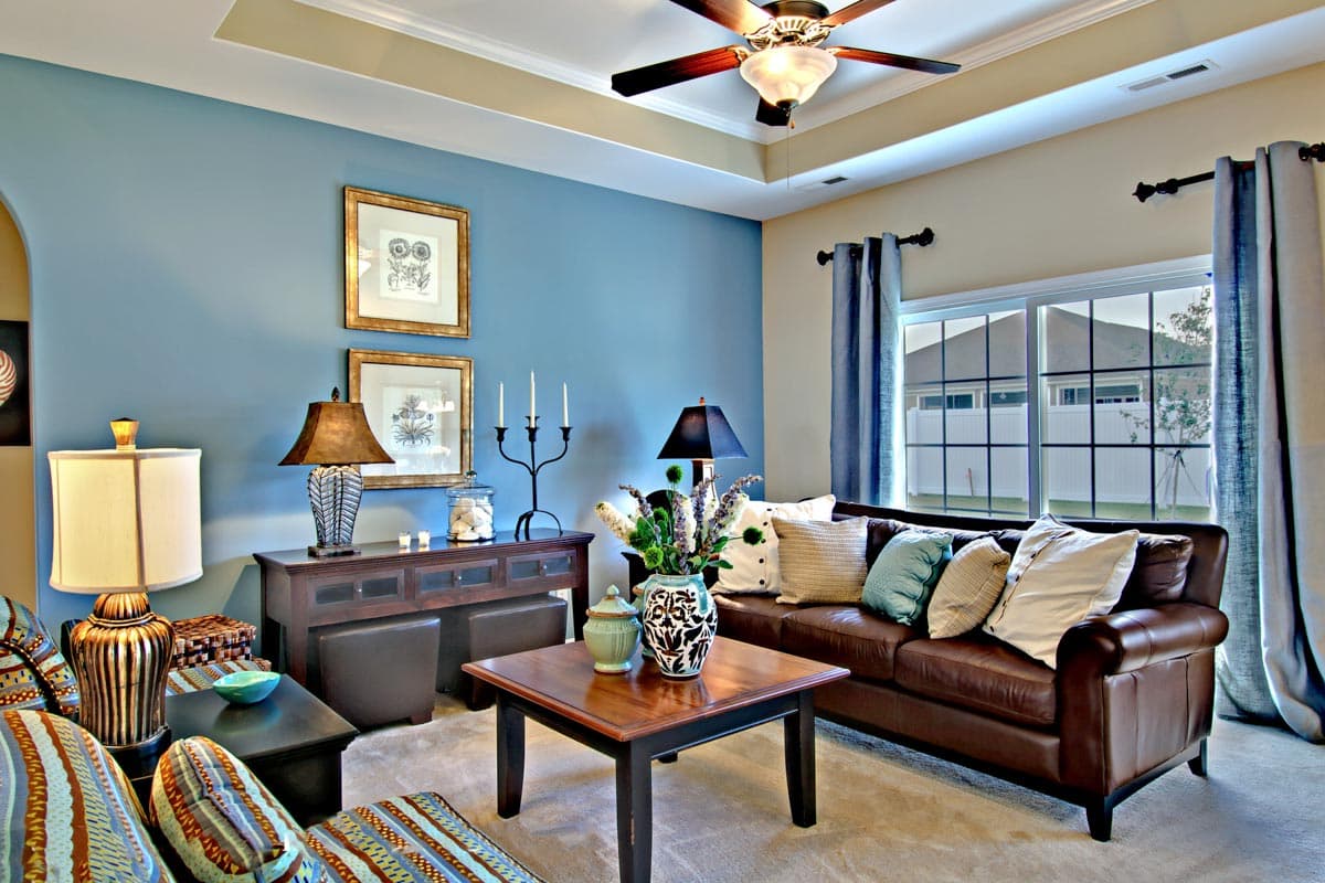 Living room with leather sofa, tray ceiling, ceiling fan, and large window overlooking a backyard.