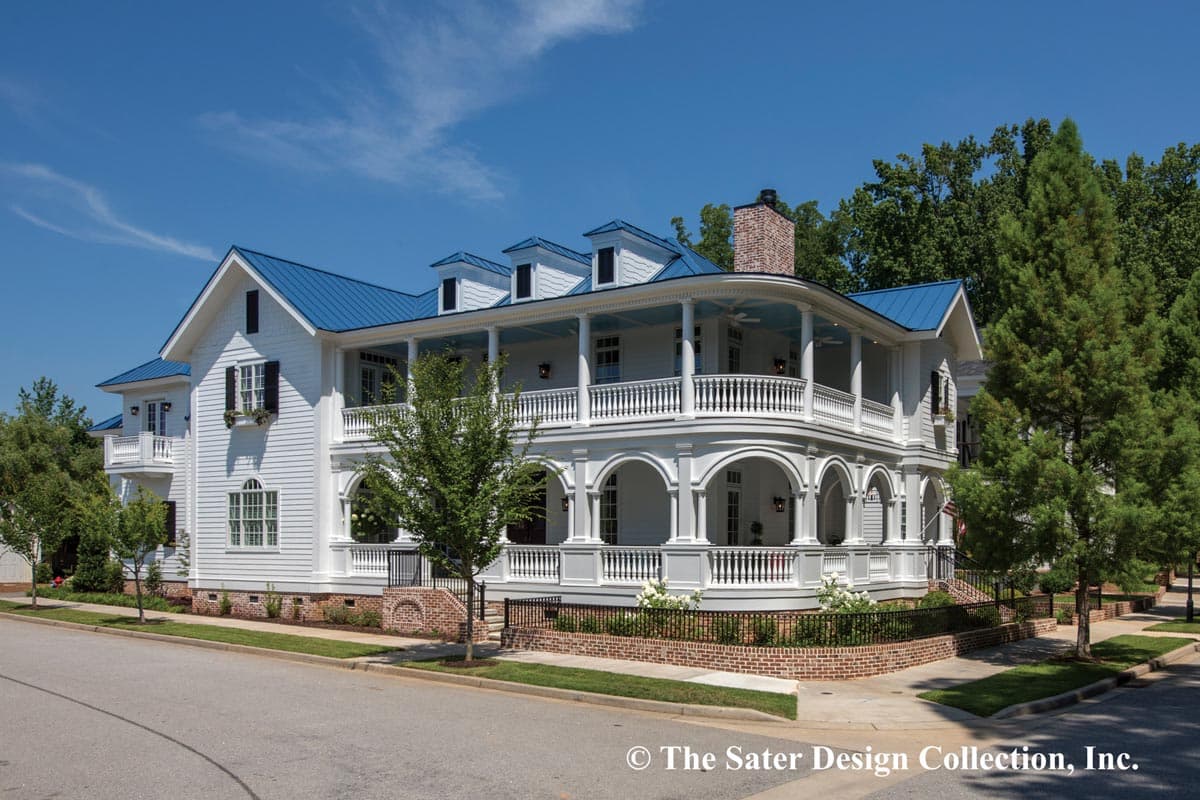 House plan exterior. Two-story Colonial-style home with a wraparound porch supported by columns, multiple dormers, and a blue metal roof.