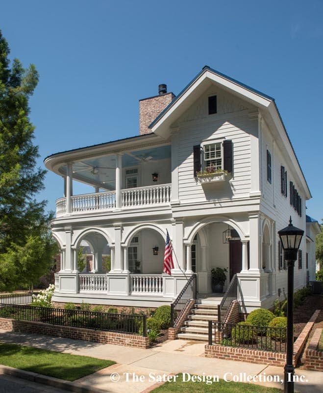 House plan exterior of a two-story home with arched entryways, a wrap-around second-floor balcony, and a prominent brick chimney.