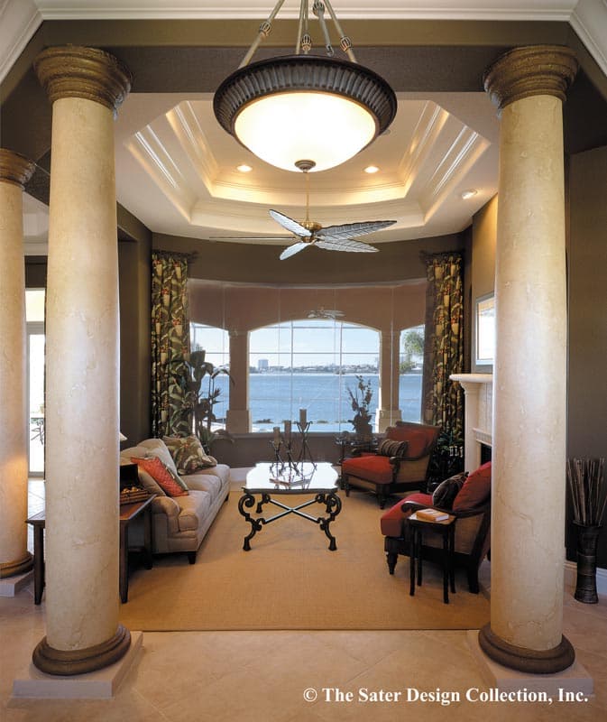 Living room with tiered ceiling, large bay window overlooking water, and Corinthian columns.