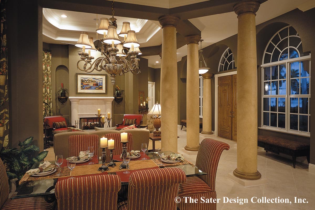 Interior view of a dining and living area with a fireplace, chandelier, and columns leading to a double door entry.