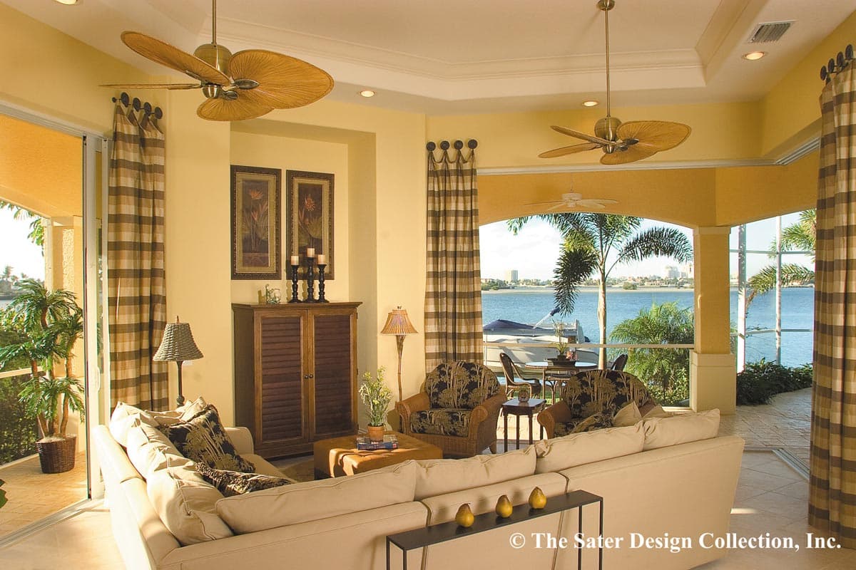Living room with large sectional sofa, wicker chairs, ceiling fans, and water view through sliding glass doors.