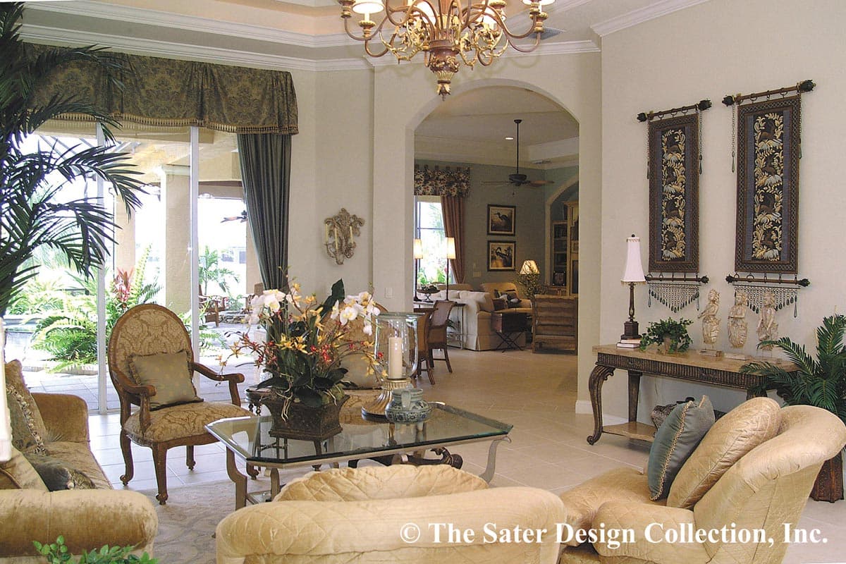 Interior view of a living room with an arched entryway to a dining area, featuring a chandelier, ornate chairs, and a glass coffee table.