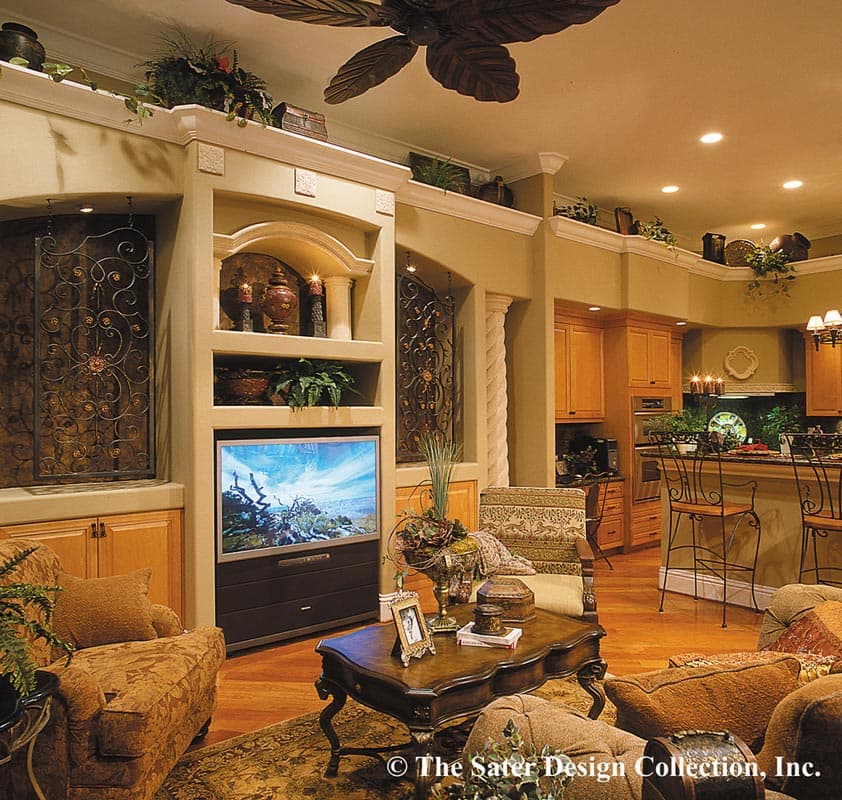 Living room with entertainment center featuring shelves, ornate metal inserts, and television. Adjacent kitchen with island and bar seating.