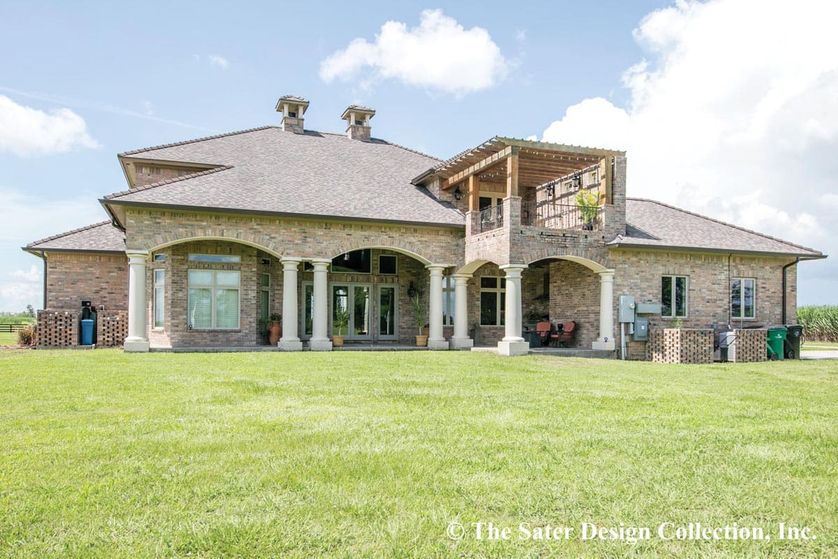 House plan exterior with brick facade, arched covered patios, balconies, and dual chimneys.