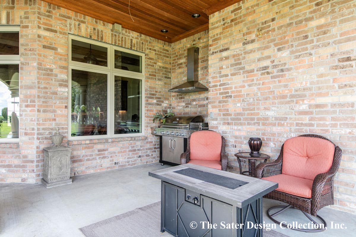 Covered outdoor patio with brick wall, stainless steel grill, two chairs, and fire pit.