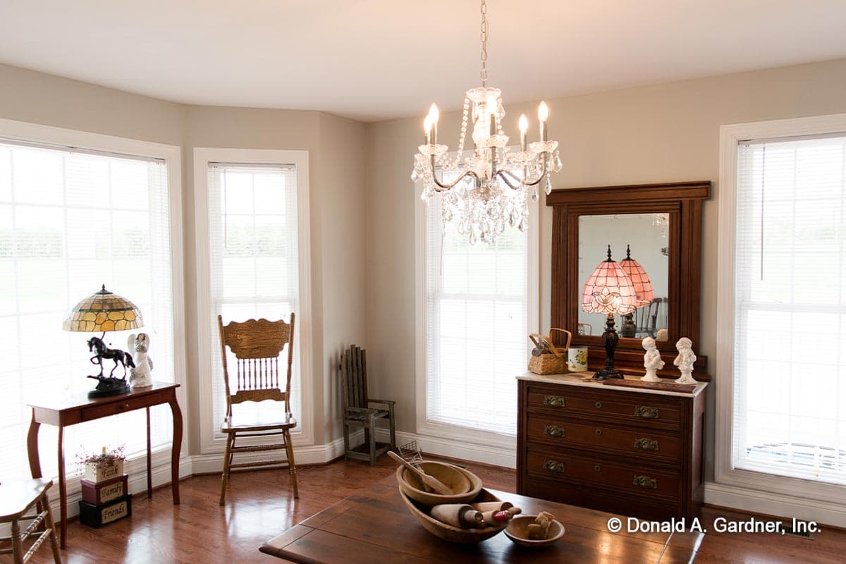 Interior view of a room with a crystal chandelier, large windows, wooden dresser with mirror, and a dining table with a bowl of rolling pins.