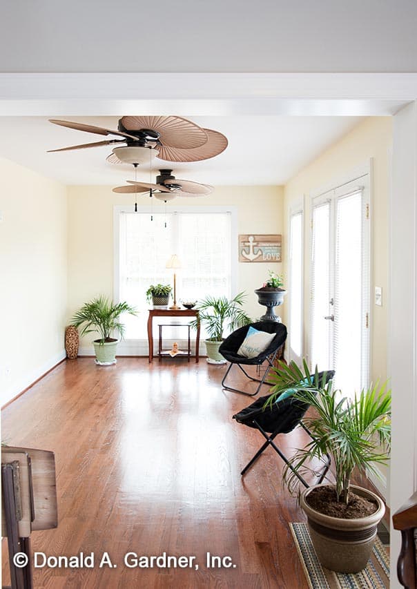 Sunroom interior with hardwood floors, two ceiling fans, and large windows. Two folding chairs and potted plants are visible.