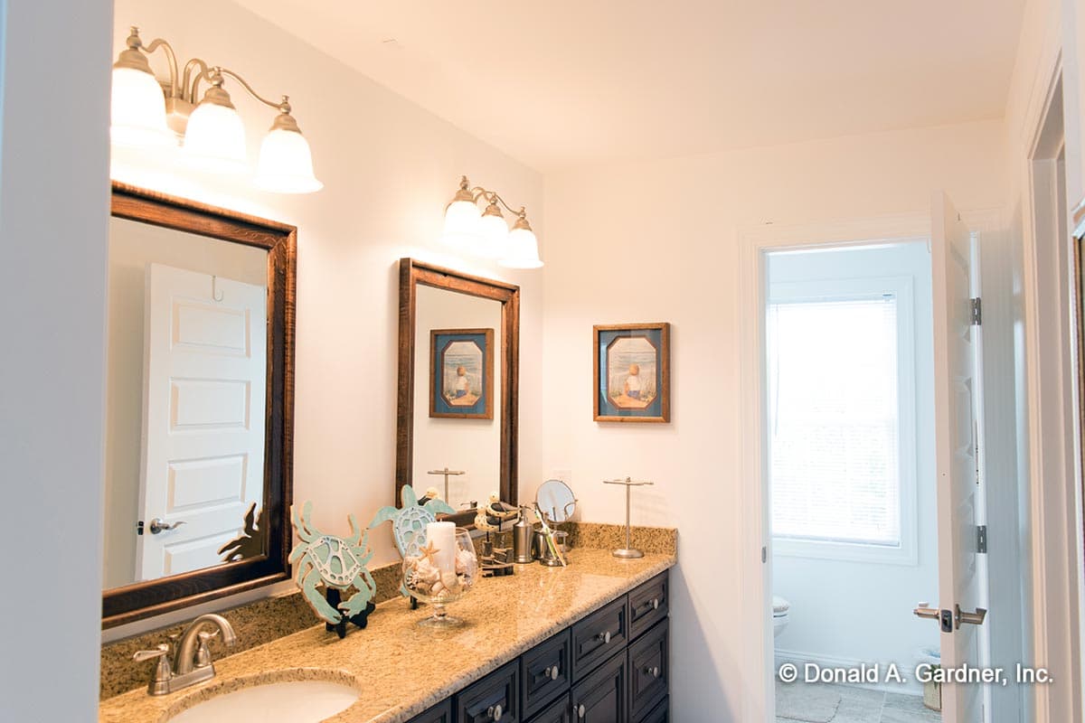 Bathroom with double vanity, granite countertop, dark wood cabinets, and two mirrors. A door leads to a room with a window and toilet.