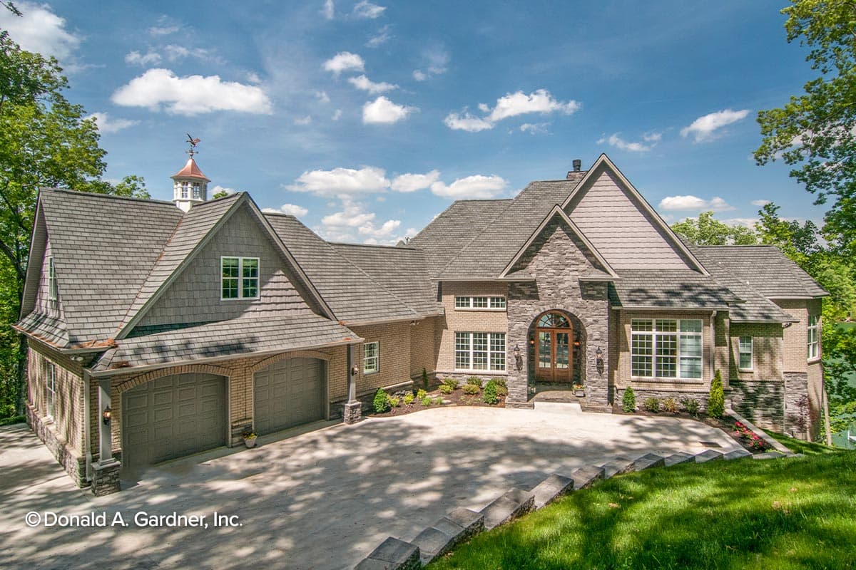House plan exterior showing a two-story home with a three-car garage, stone accents, arched entry, and cupola.