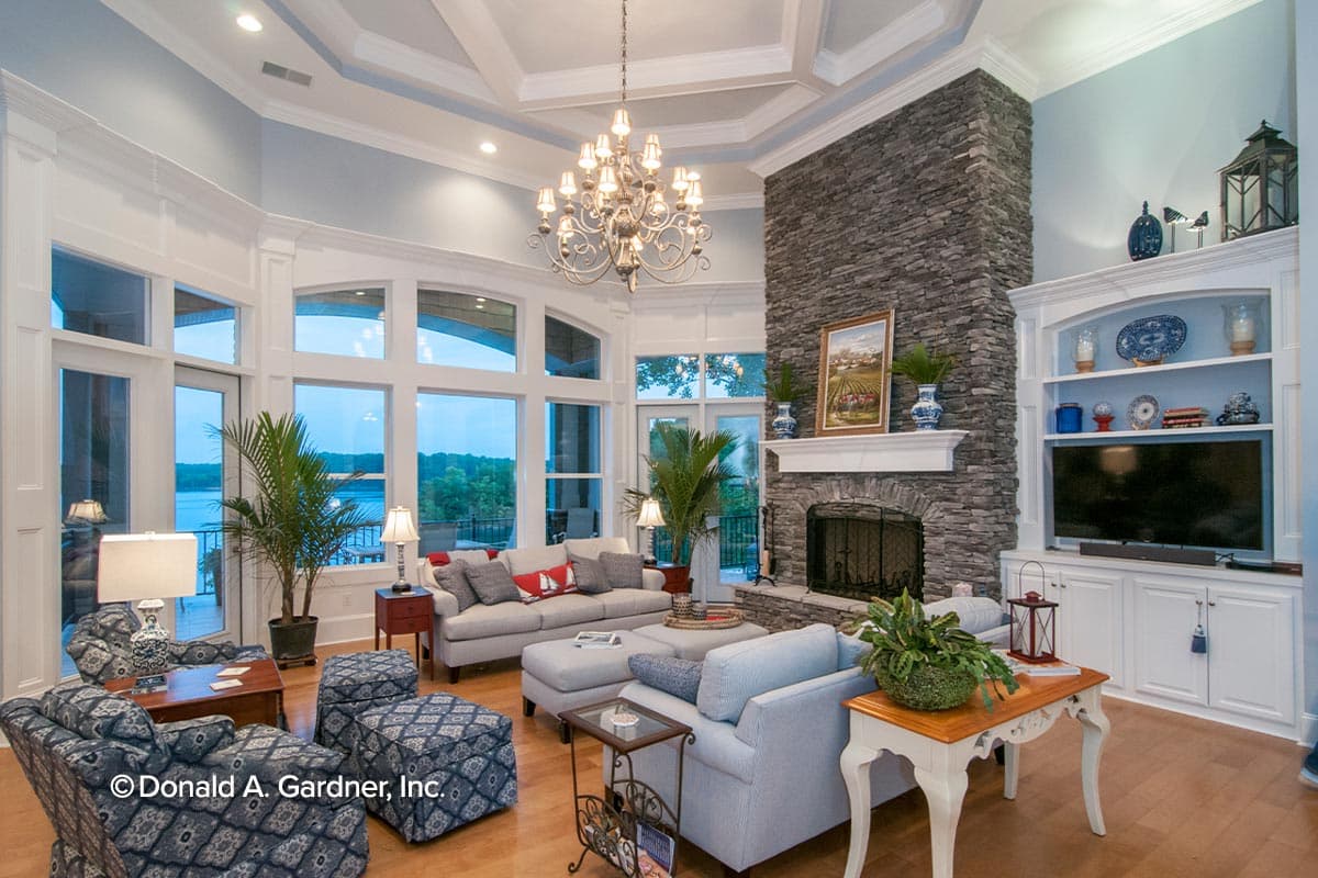 Great room interior with stone fireplace, coffered ceiling, large windows overlooking water, and built-in entertainment center.
