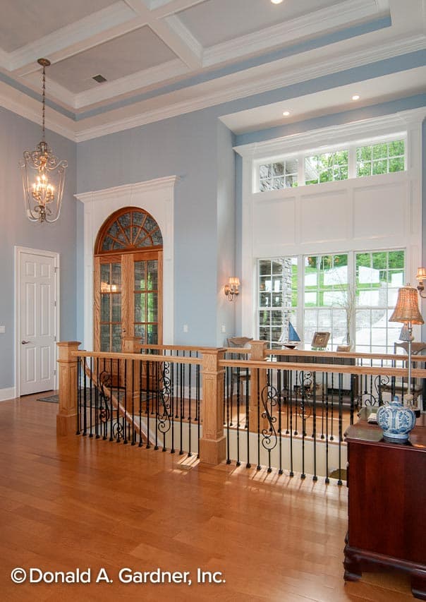 Interior view: second floor landing with coffered ceiling, arched wood doors, and tall windows. Oak railing with wrought iron balusters.
