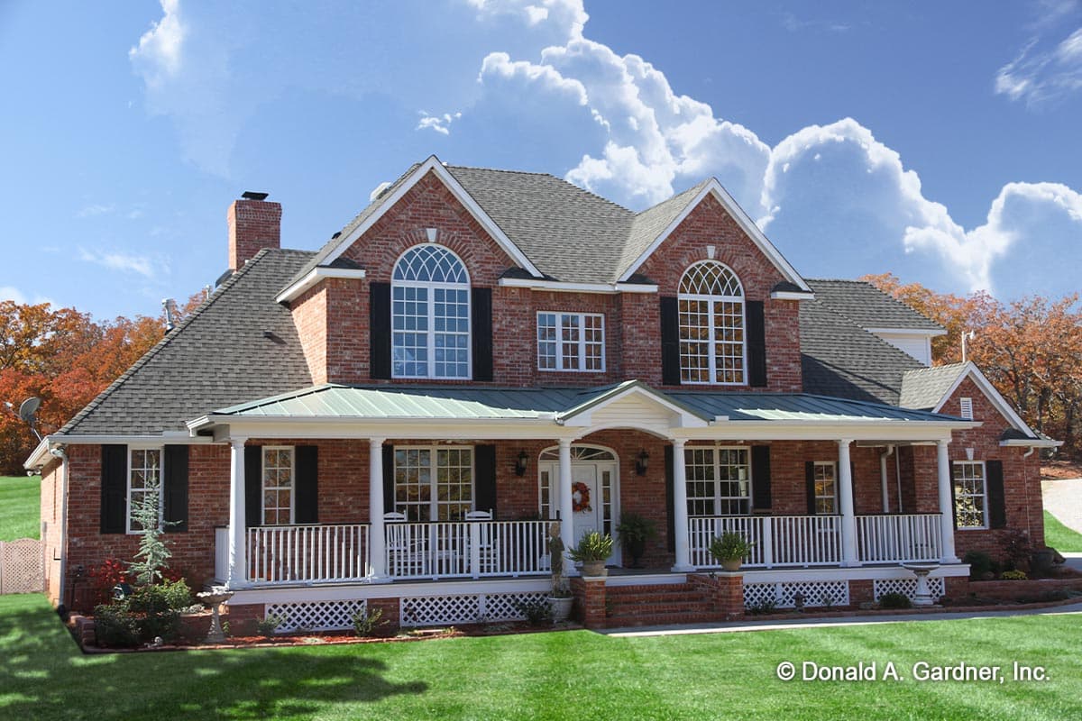 House plan exterior. Two-story Colonial-style home with a wraparound porch, gabled roof, and arched windows.