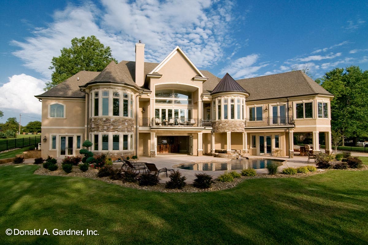 House plan exterior: Two-story home with stone accents, turrets, multiple gables, a rear balcony, and a pool.