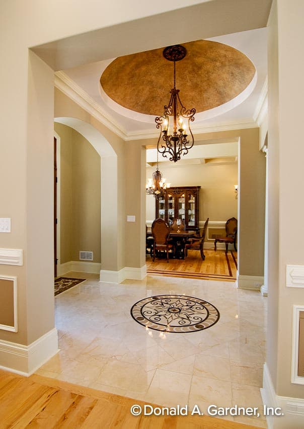 Entry foyer with marble floor inlay and tray ceiling with chandelier, opening to dining room with hutch.