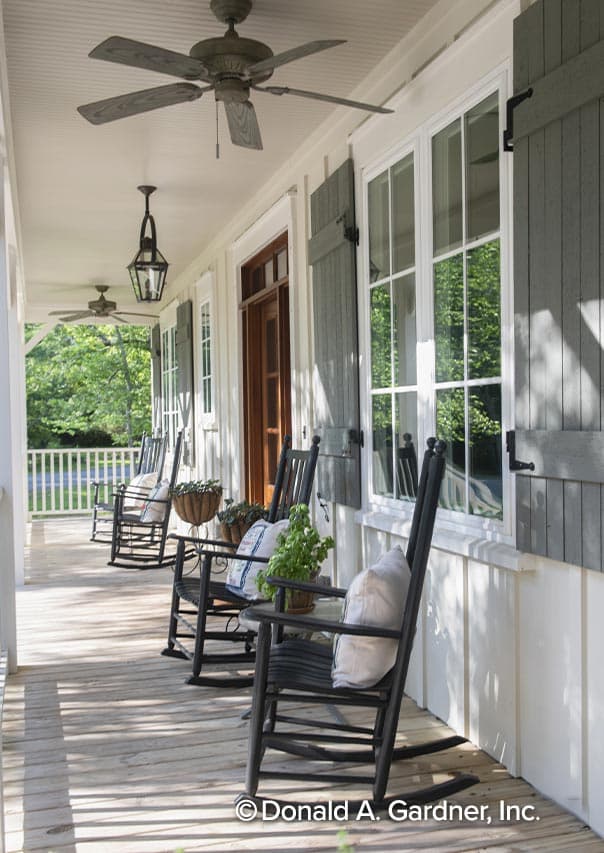 House plan exterior: Covered porch with rocking chairs, white railing, ceiling fans, and pane windows with gray shutters.