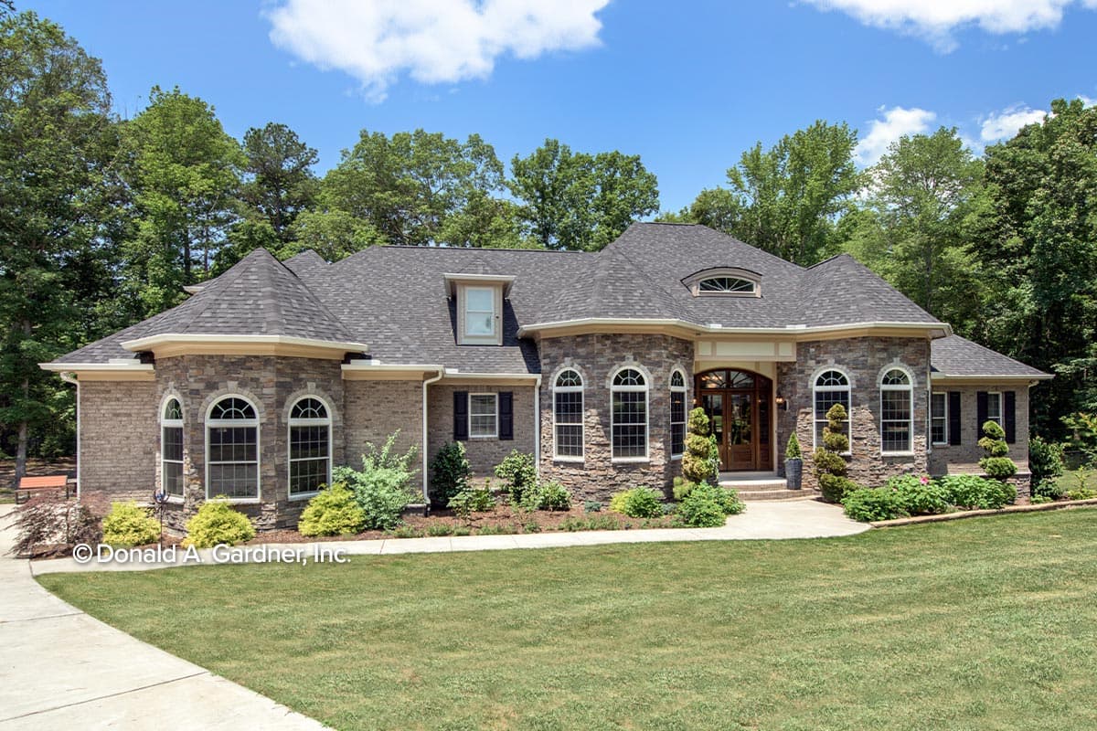 House plan exterior. Two-story home with a stone and brick facade, a multi-gabled roof, arched windows, and a portico with a wood door.