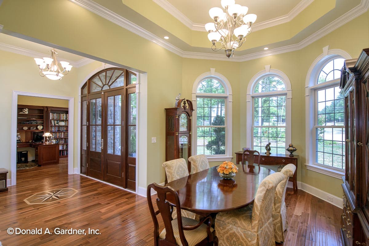 Dining room with oval table, arched windows, grandfather clock, and view into office with built-in bookshelves.