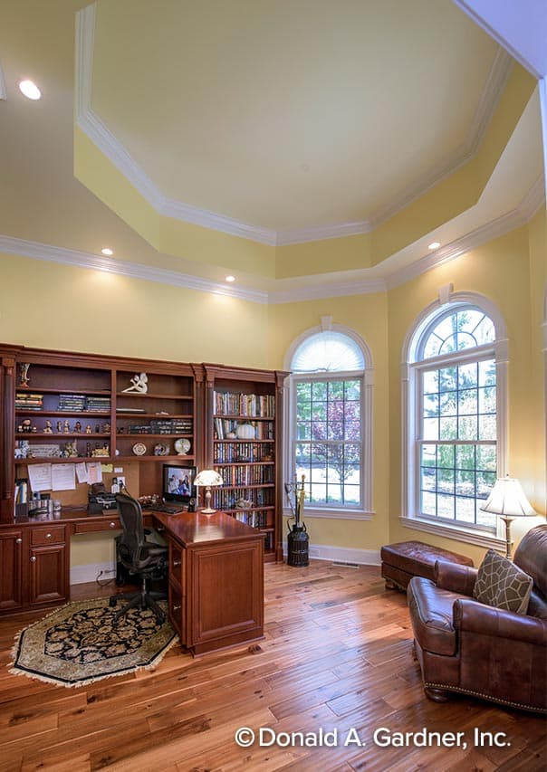 Home office with built-in bookshelves, desk, armchair, and octagonal coffered ceiling with recessed lighting.