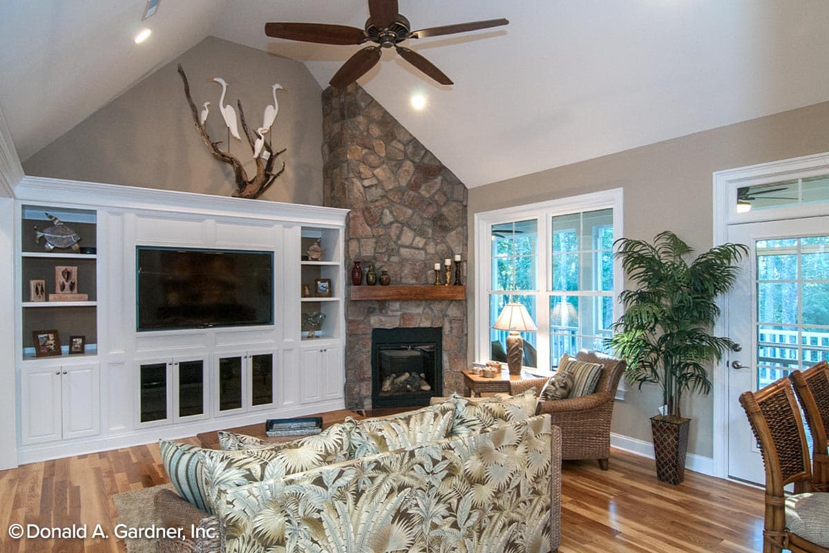 Interior view of living room with vaulted ceiling, stone fireplace, built-in entertainment center, and large windows.