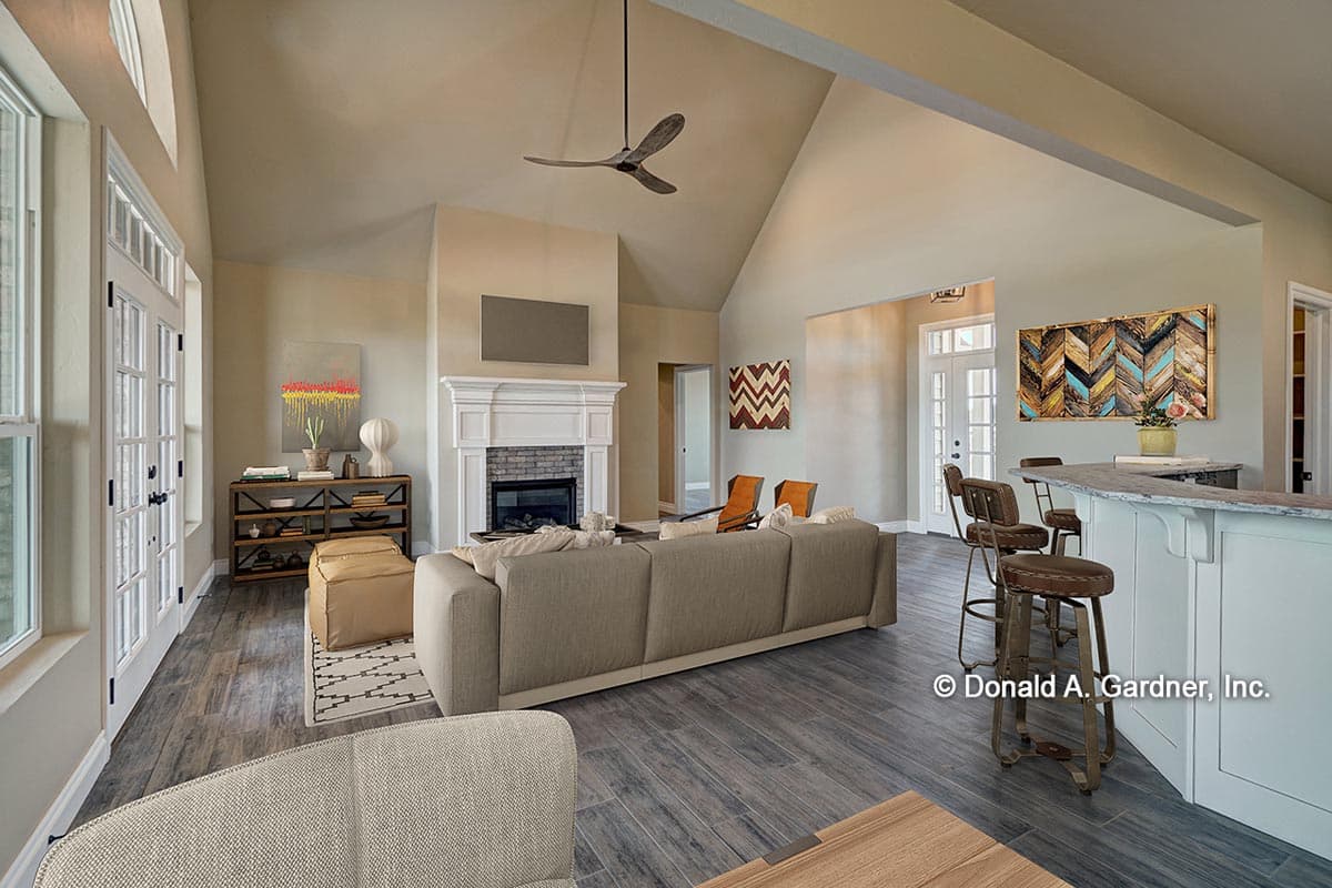 Great room with vaulted ceiling, stone fireplace, and large windows. Bar area visible.