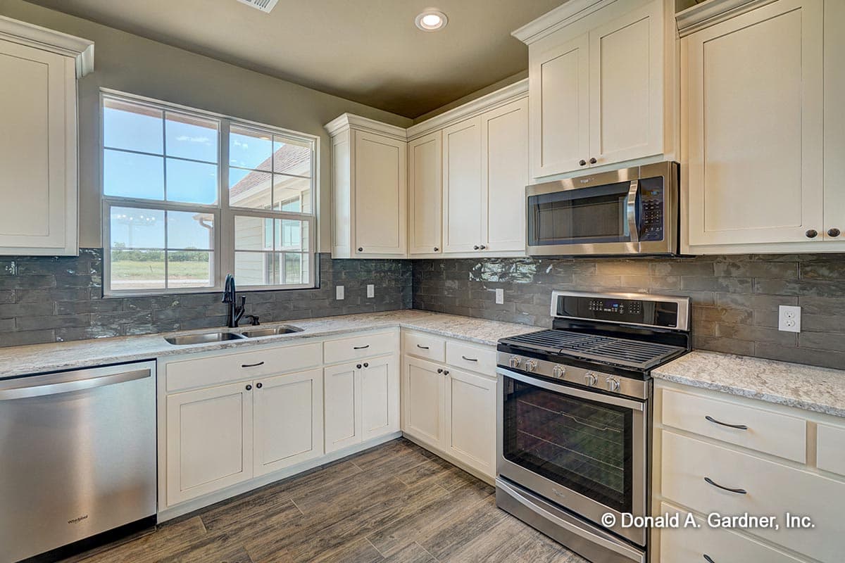 Kitchen with white cabinets, granite countertops, dark subway tile backsplash, stainless steel appliances, and large double-hung window.