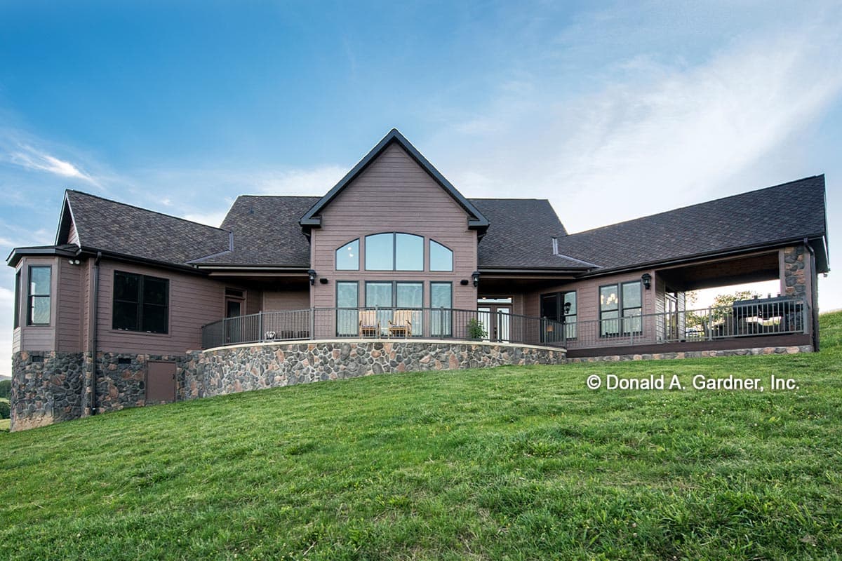 House plan exterior: Modern style, two stories, gabled central section with arched window, stone foundation, and covered deck.