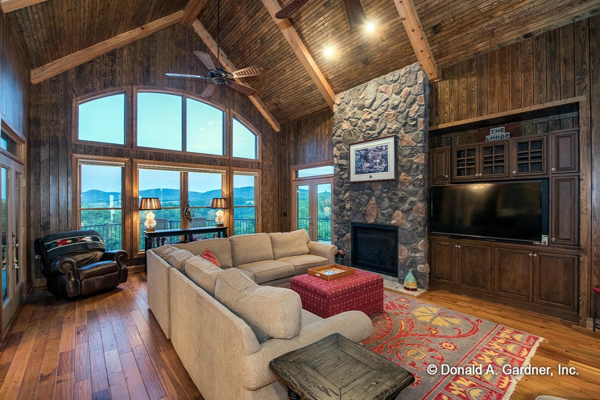 Living room with vaulted wood-paneled ceiling, stone fireplace, entertainment center, and large windows with mountain views.