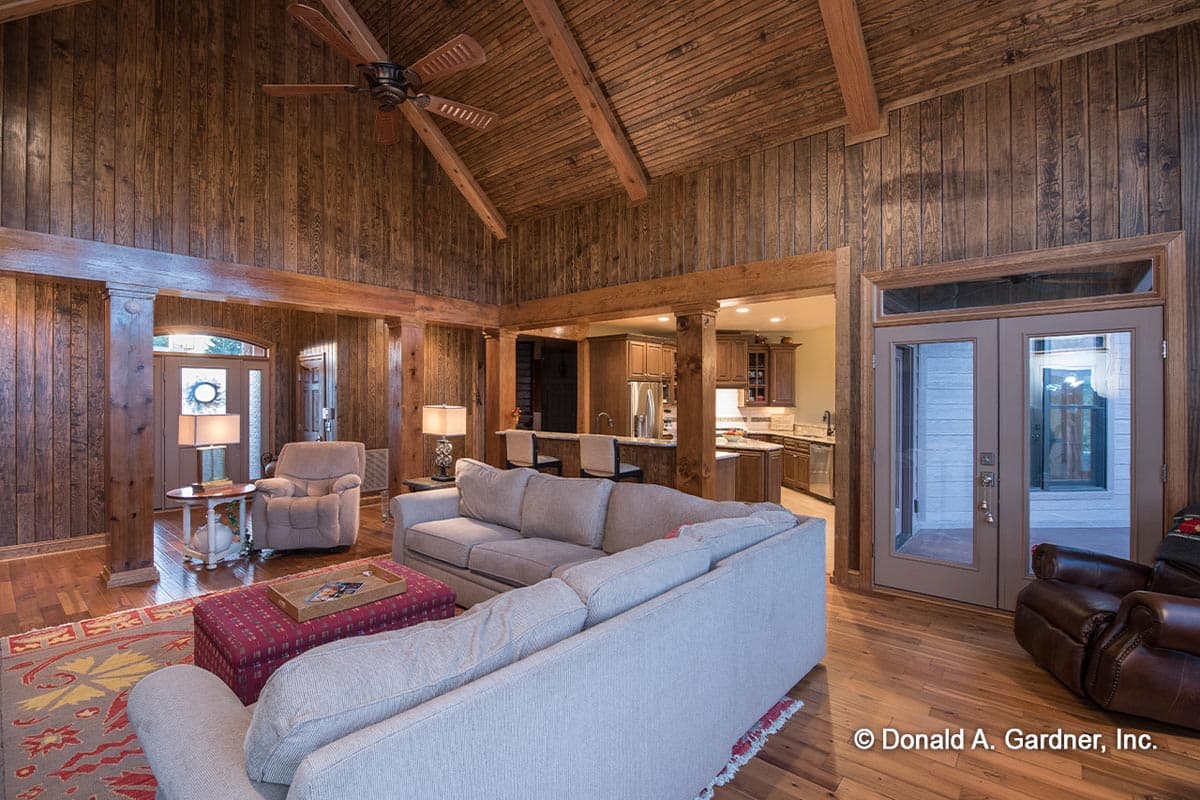 Living area with vaulted, beamed ceiling, wood paneling, open to kitchen with island, and double doors to exterior.