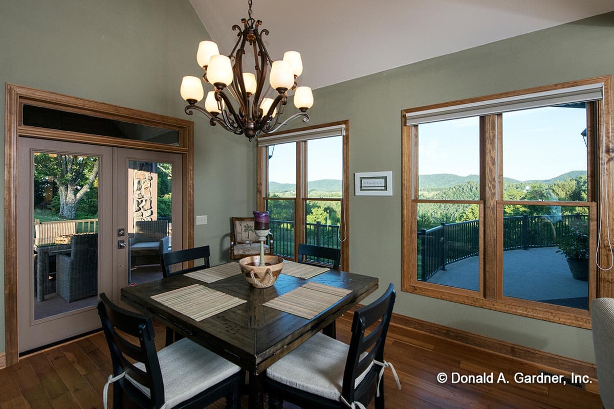 Dining room with wooden table, chairs, chandelier, double doors to patio, and large windows with mountain views.