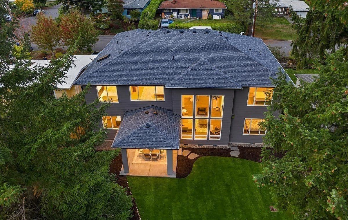 House plan exterior, two stories, modern style, dark siding, prominent gabled roof, covered patio, and large windows.