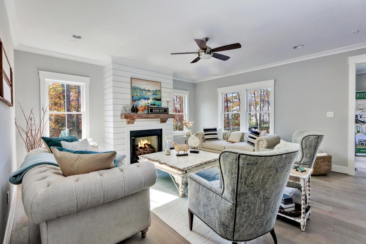 Interior view of living room with shiplap fireplace, mantel, and large windows overlooking trees.