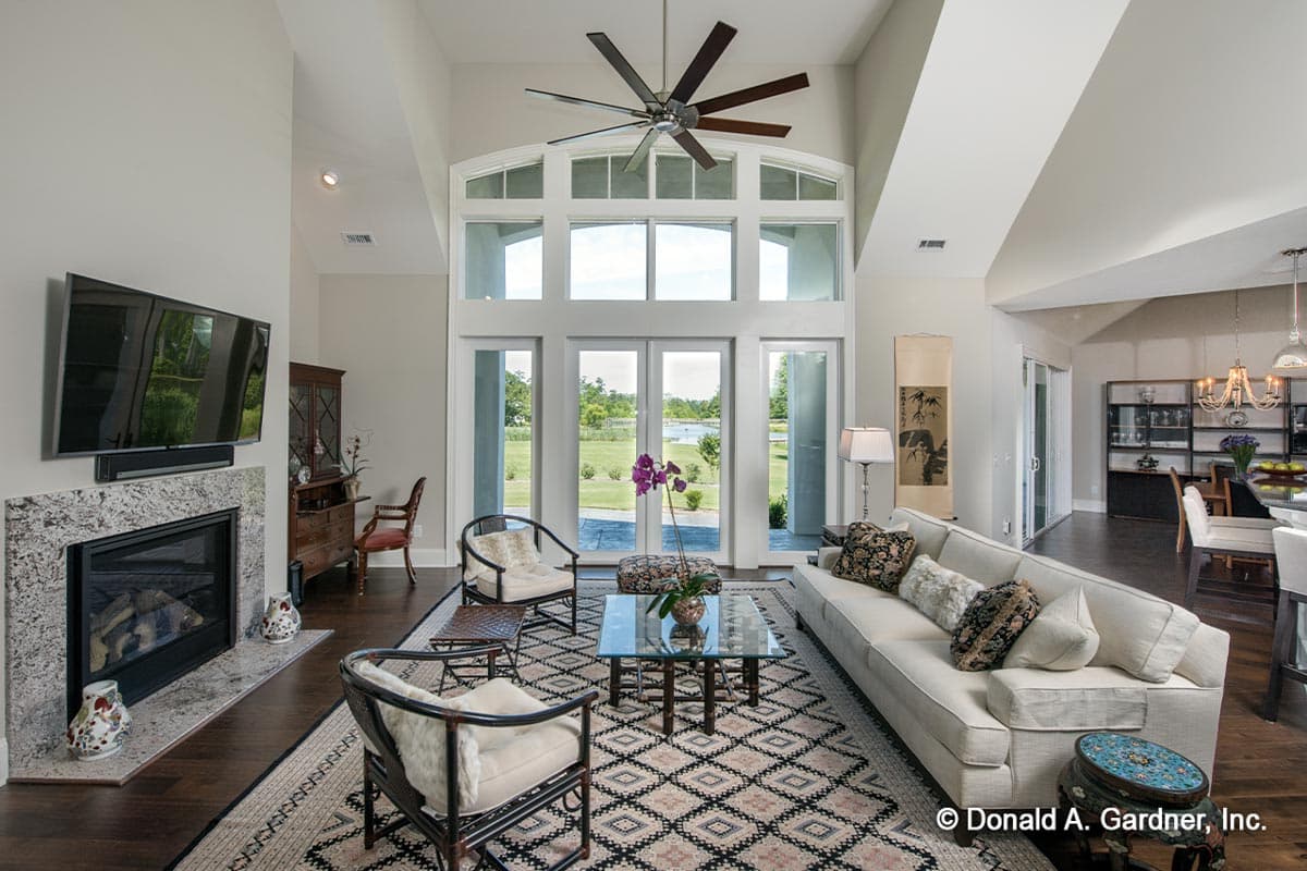 Interior view of living room with fireplace, vaulted ceiling, large windows, and view of a lake.