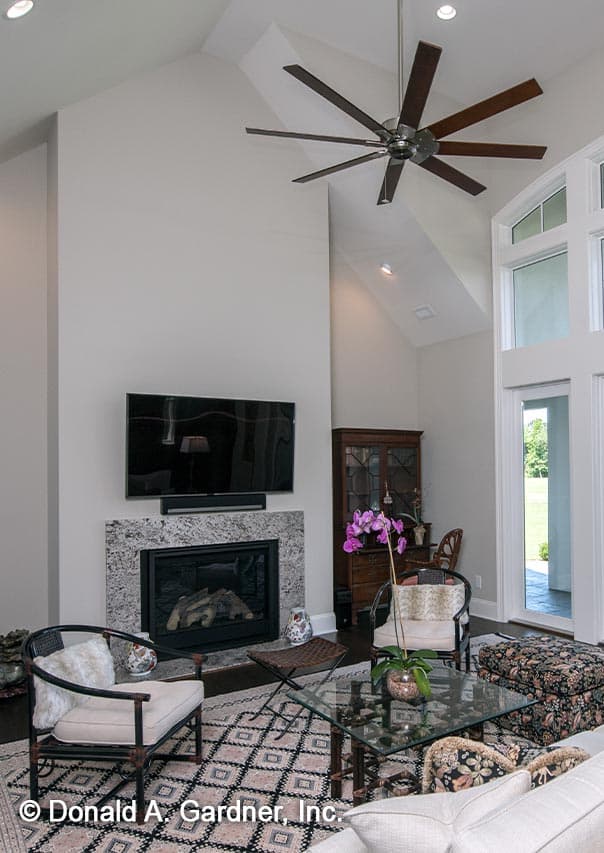 Living room with vaulted ceiling, fireplace, large windows, and a multi-blade ceiling fan.