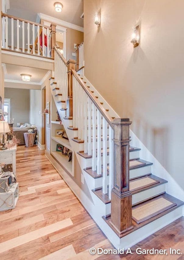 Interior view of a staircase with built-in shelving, white balusters, and wooden newel posts.