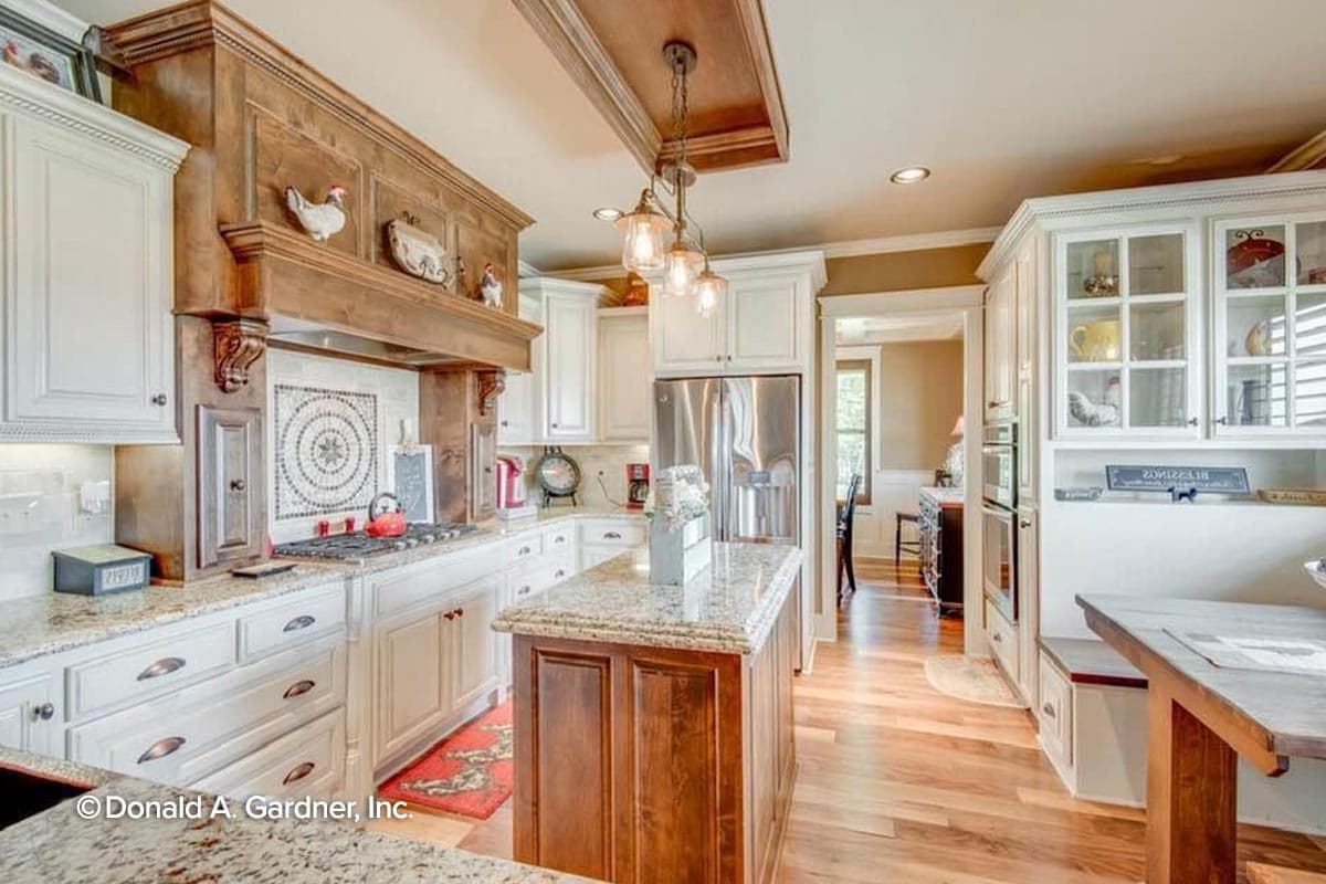 Kitchen with a large wooden range hood, island with granite countertop, white cabinetry, and stainless steel appliances.