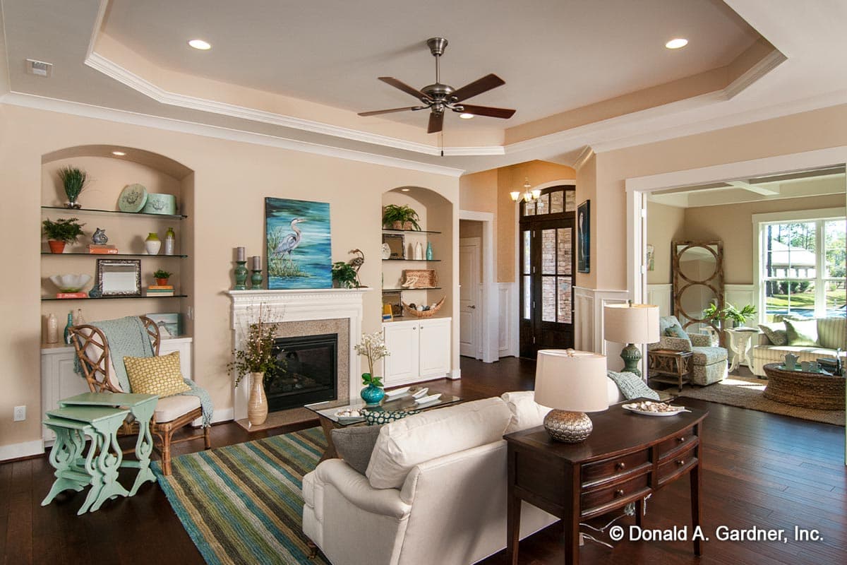 Interior view of a living room with a fireplace, built-in shelving, ceiling fan, and an open doorway to another room.