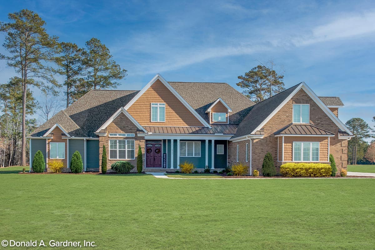 House plan exterior. Two-story with a combination of brick and wood siding. Features include a front porch, multiple dormers, and gabled rooflines.