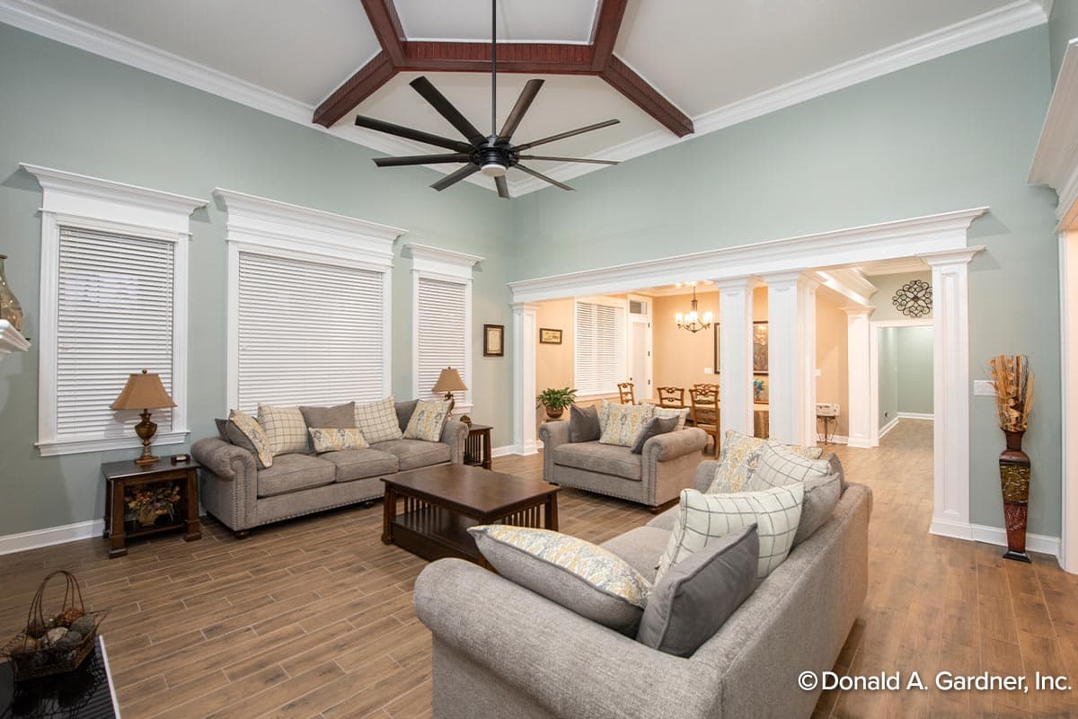 Living room with coffered ceiling, decorative beams, large ceiling fan, and view into dining room.