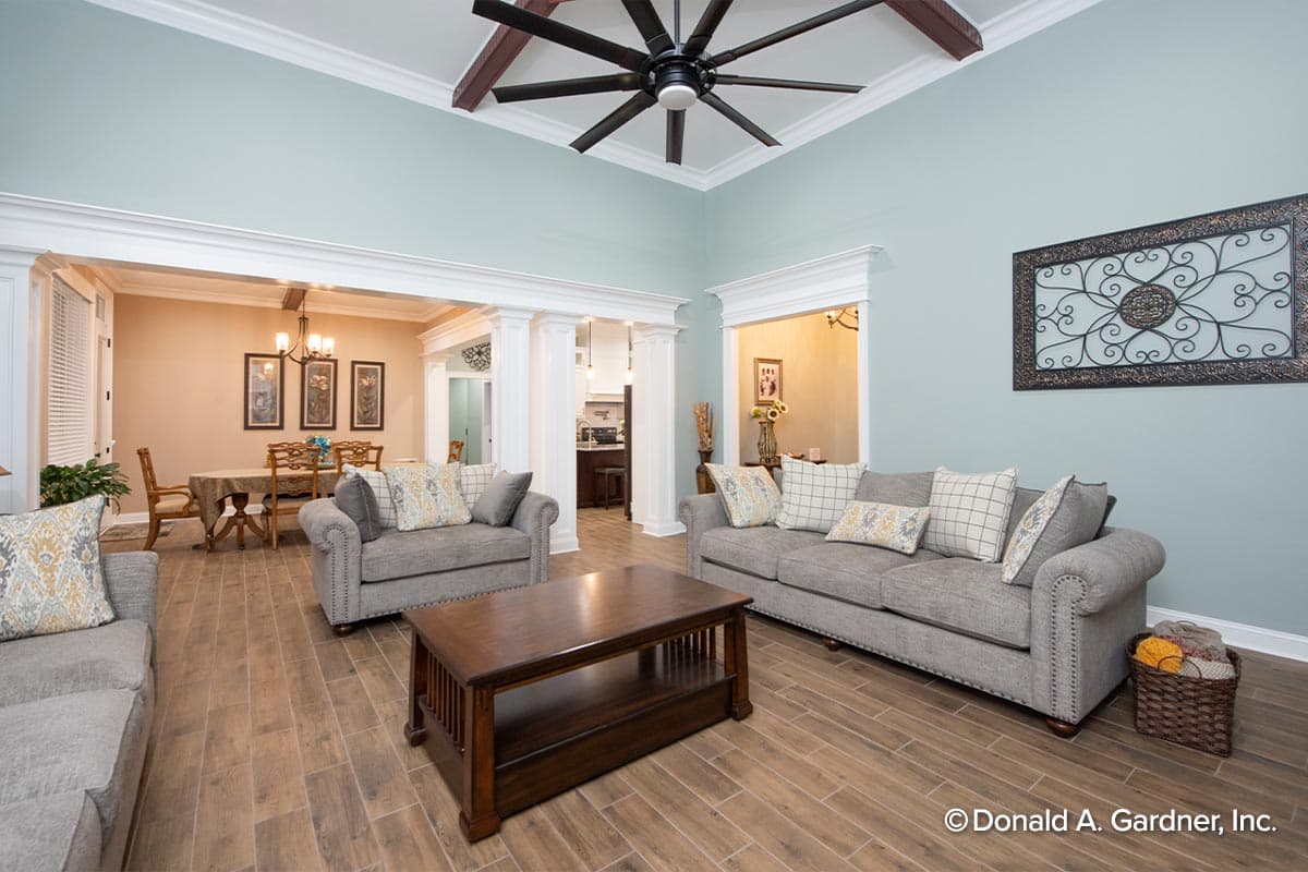 Living room with vaulted ceiling, exposed beams, and view into dining room and kitchen.