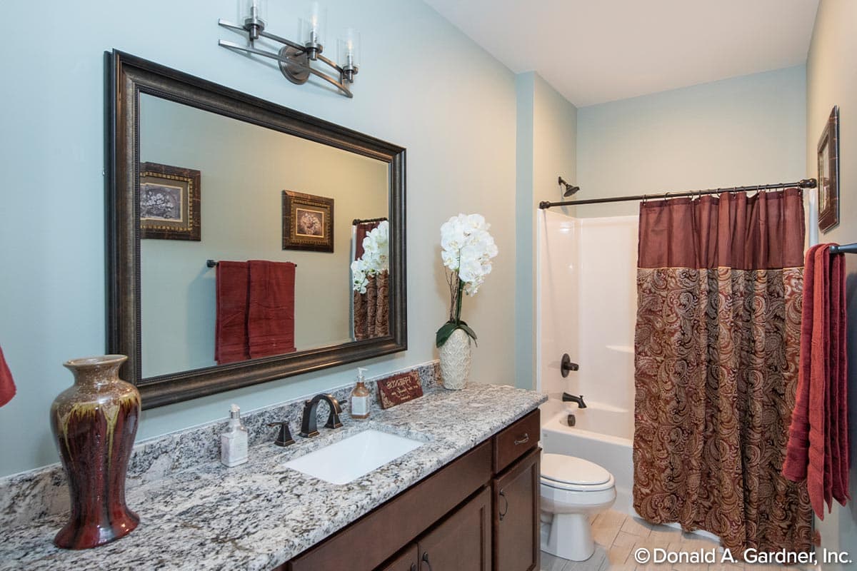 Bathroom featuring a vanity with granite countertop, sink, large mirror, and a bathtub with a decorative shower curtain.