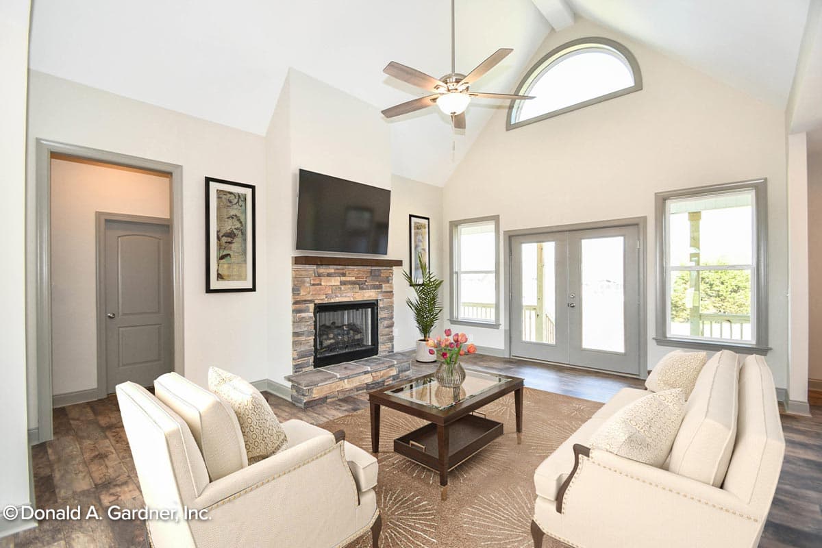 Great room with stone fireplace, vaulted ceiling, arched window, and double doors to the exterior.